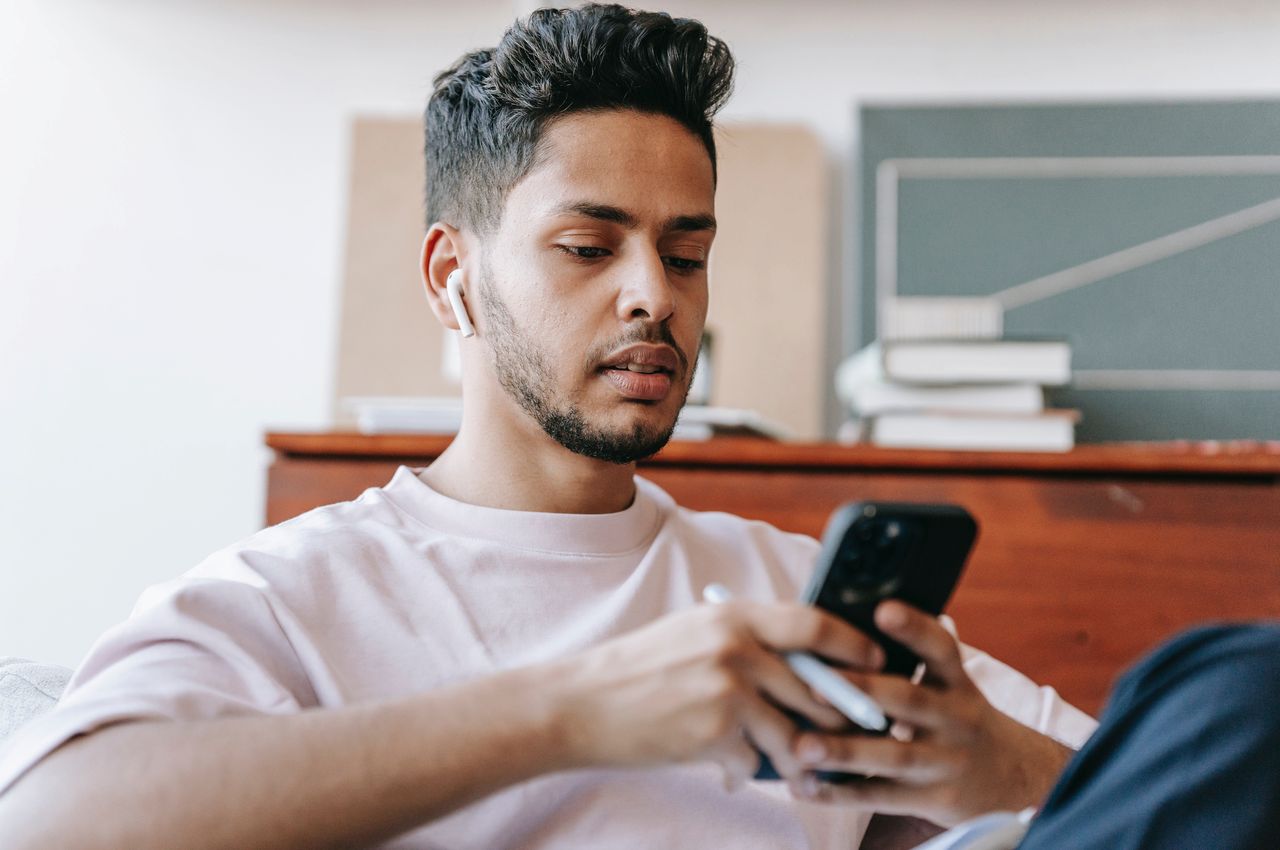 A imagem mostra um homem usando fones de ouvido e usando seu celular.