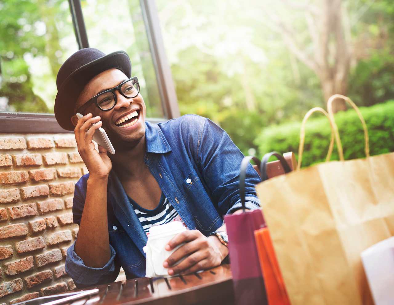 A imagem mostra um homem usando um chapéu preto e blusa listrada, falando ao telefone. Ele está sorridente.