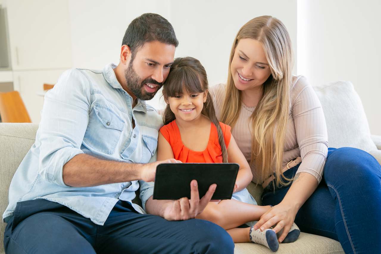 A imagem mostra um casal com sua filha, usando um tablet. Todos estão sorridentes.