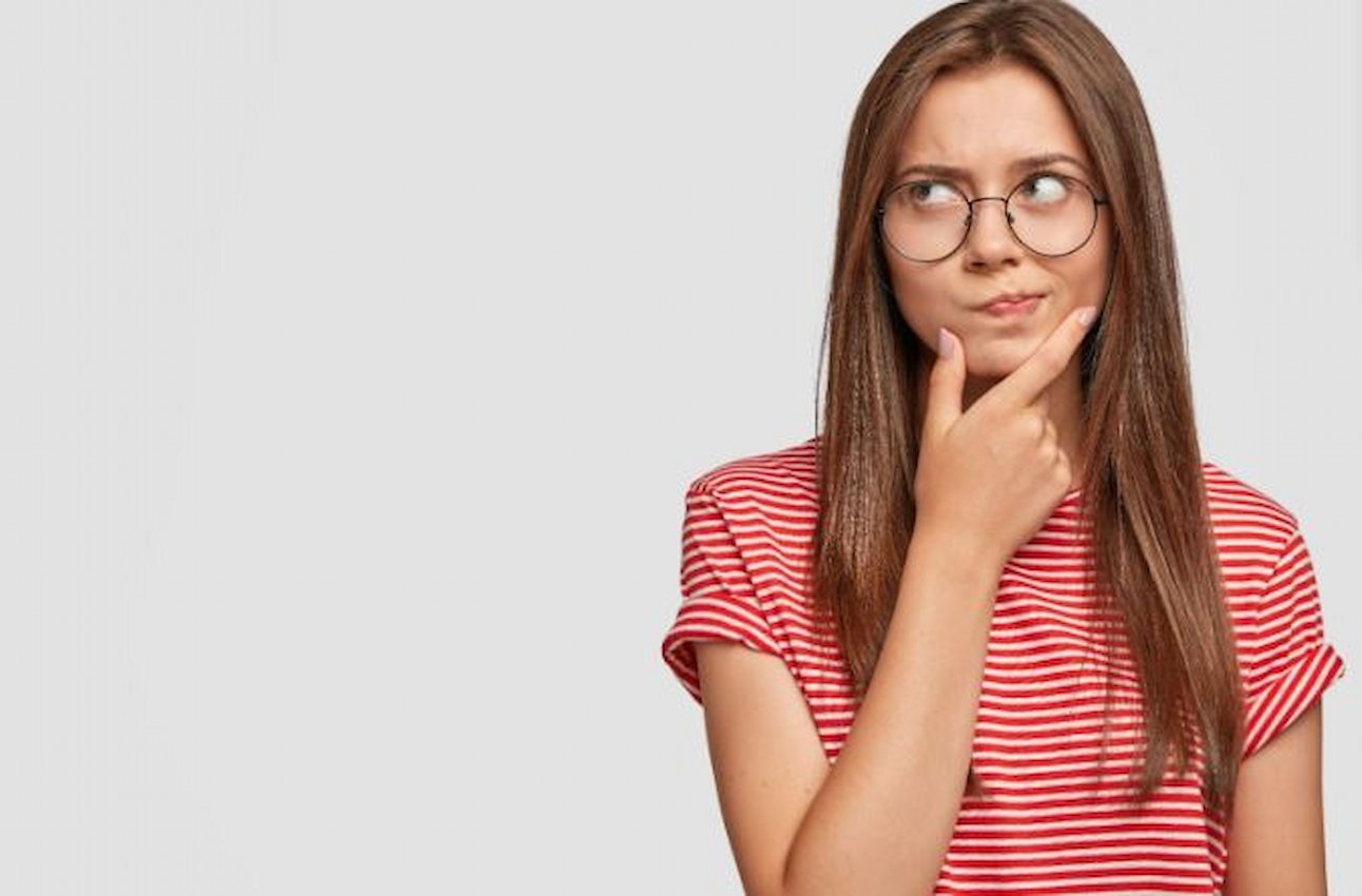 A imagem mostra uma mulher usando blusa vermelha, usando óculos. Ela aparenta estar pensativa.