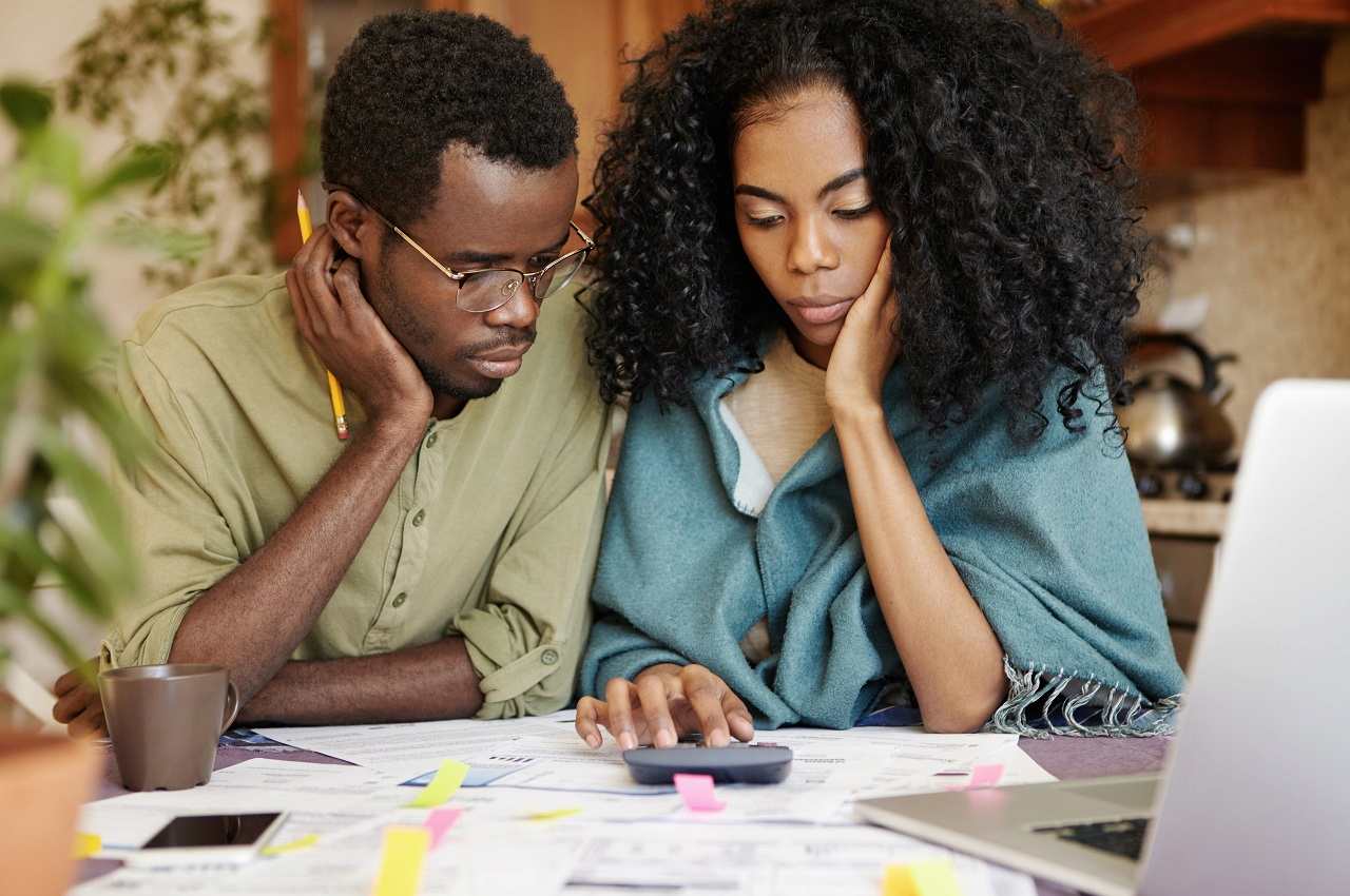 A imagem mostra um casal fazendo contas na calculadora. 