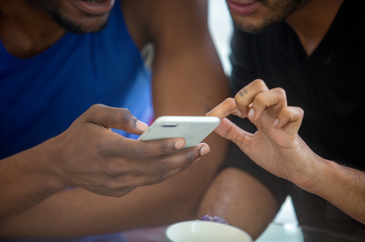 Dois homens acessando conta-corrente pelo mesmo celular (seus rostos não aparecem na imagem). 