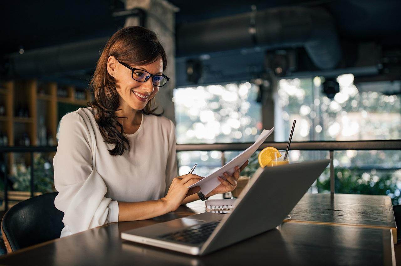 A imagem mostra uma mulher sorridente trabalhando em seu escritório.