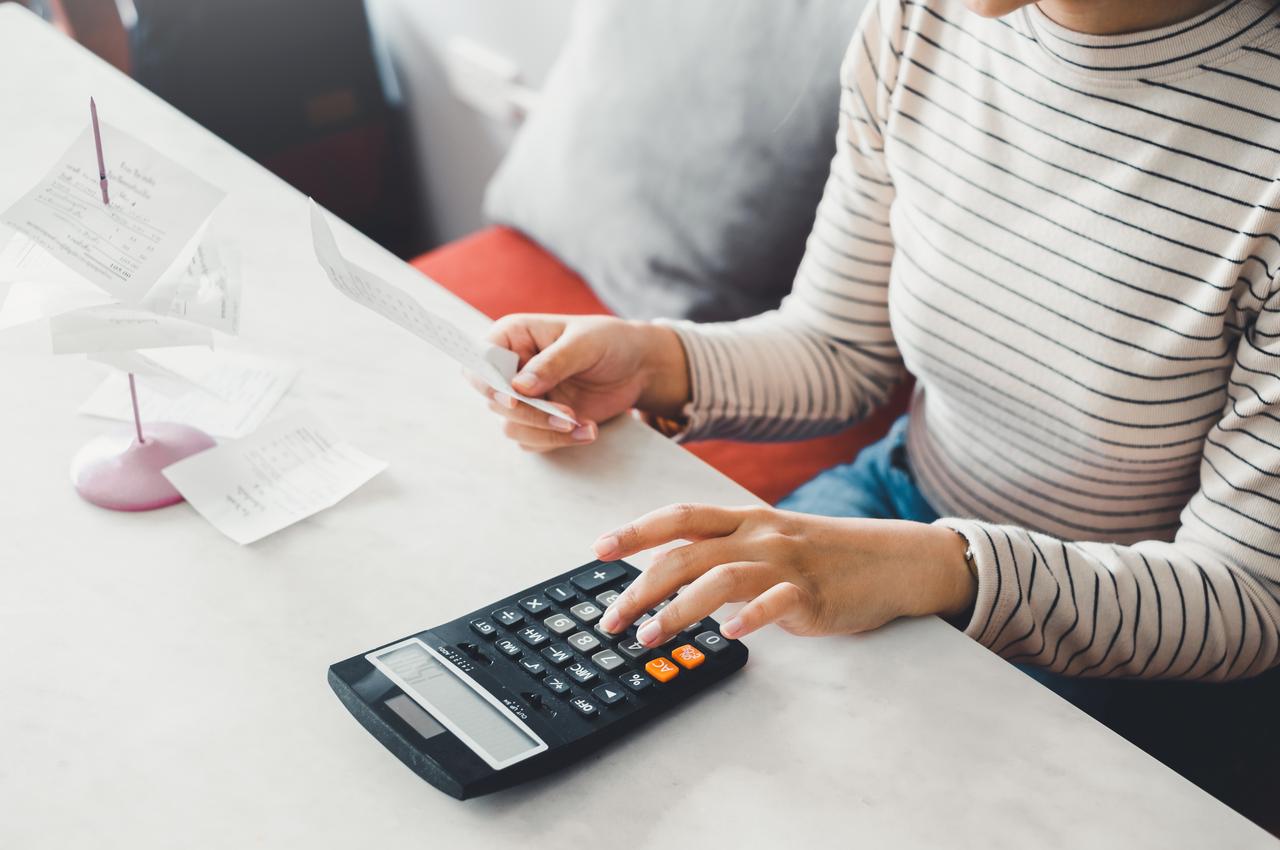 Mulher com blusa listrada preta e branca, utilizando calculadora e segurando notas fiscais.