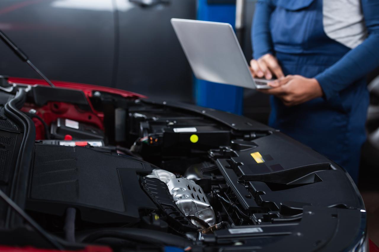 Mecânico usando um notebook enquanto realiza a inspeção do motor de um carro durante a vistoria veicular.