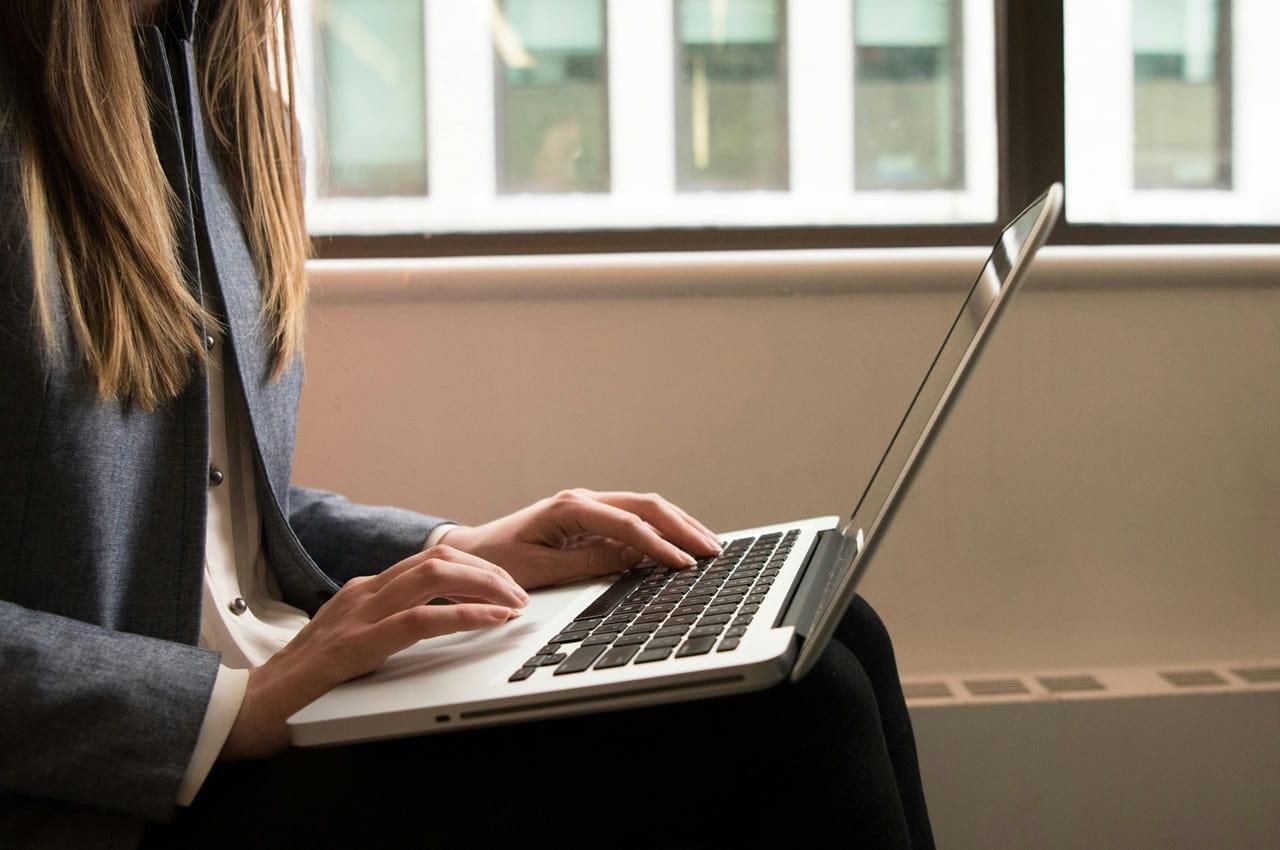 Mulher sentada com um notebook apoiado em suas pernas. Ela pesquisando sobre o Renave de veículos.