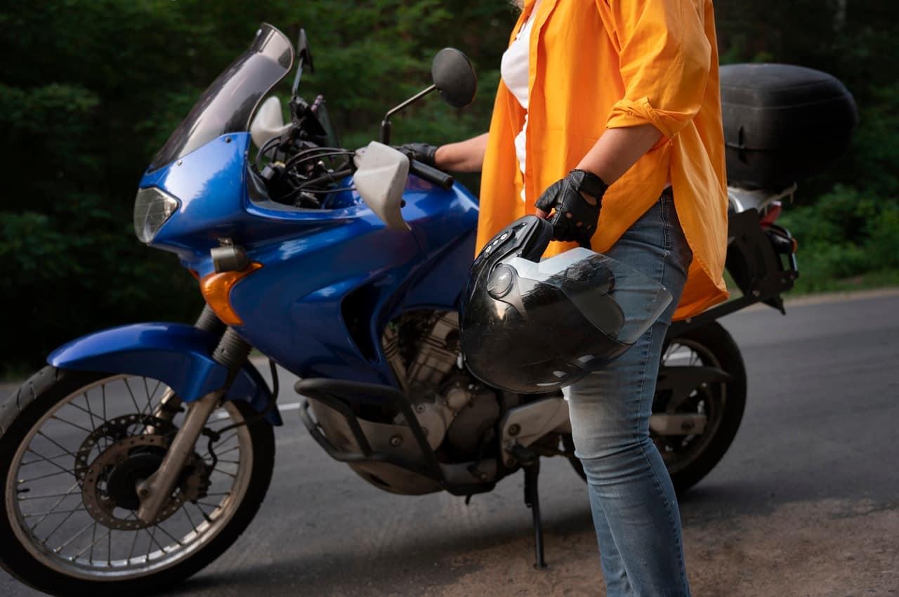 Pessoa em uma moto azul segurando um capacete em uma de suas mãos.