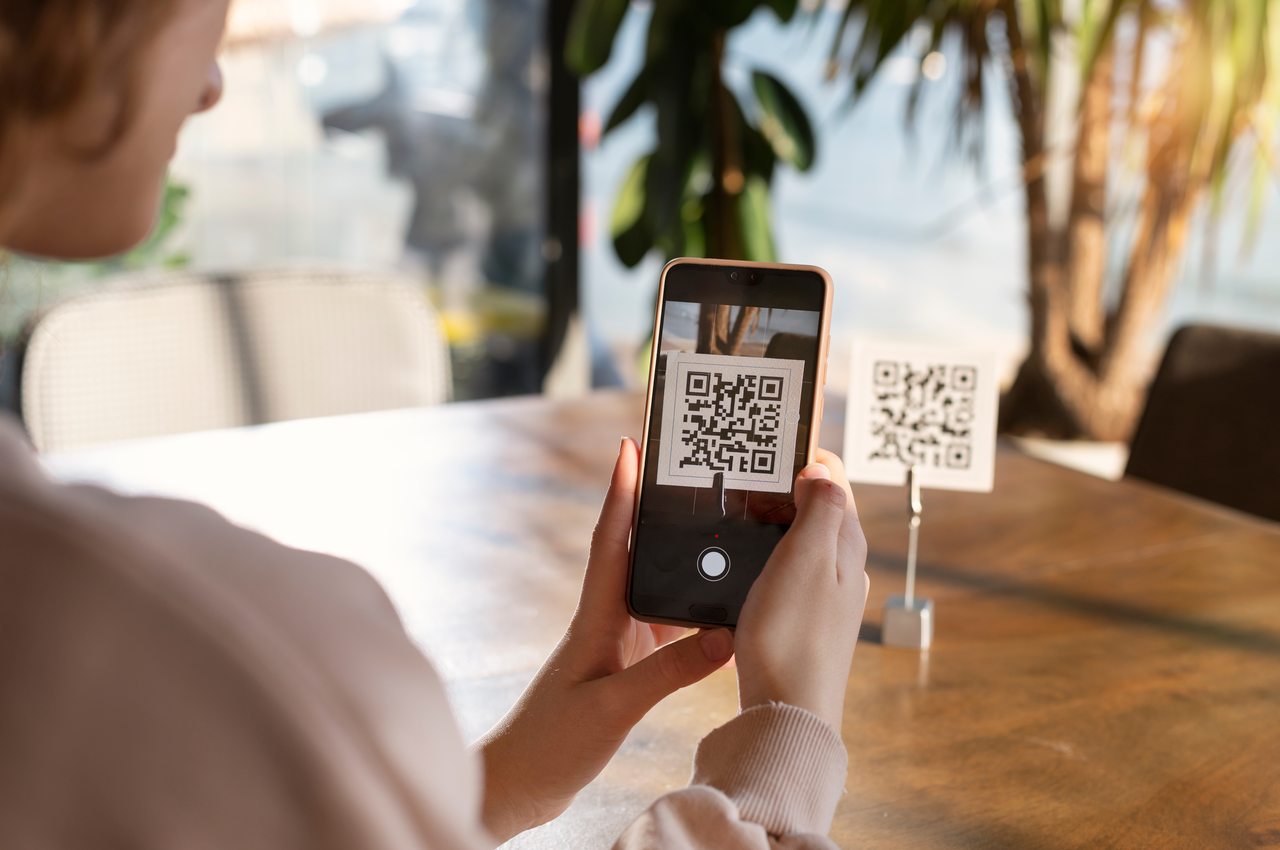 Mulher (seu rosto não aparece na imagem) pagando conta de restaurante com o celular por meio de um QR Code