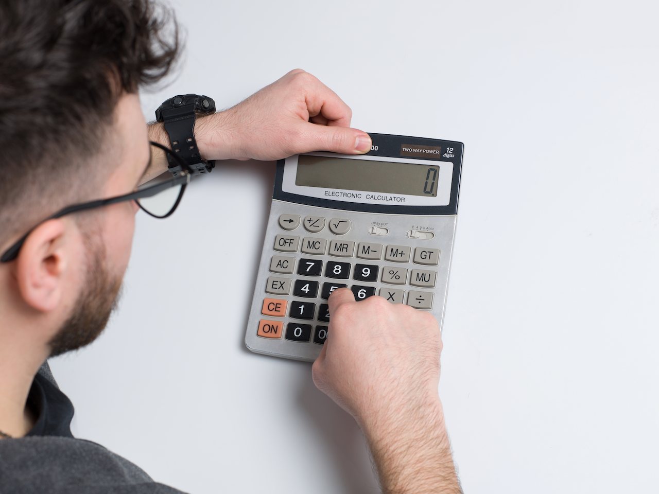 A imagem mostra um homem realizando contas em uma calculadora.