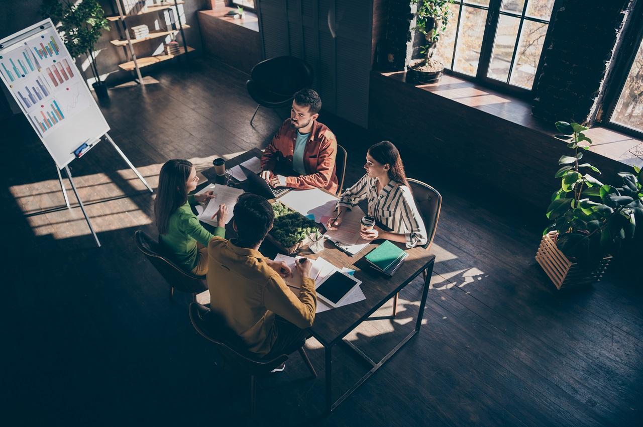 Grupo de pessoas conversando enquanto estão sentados em uma mesa do trabalho analisando resultados em gráficos.