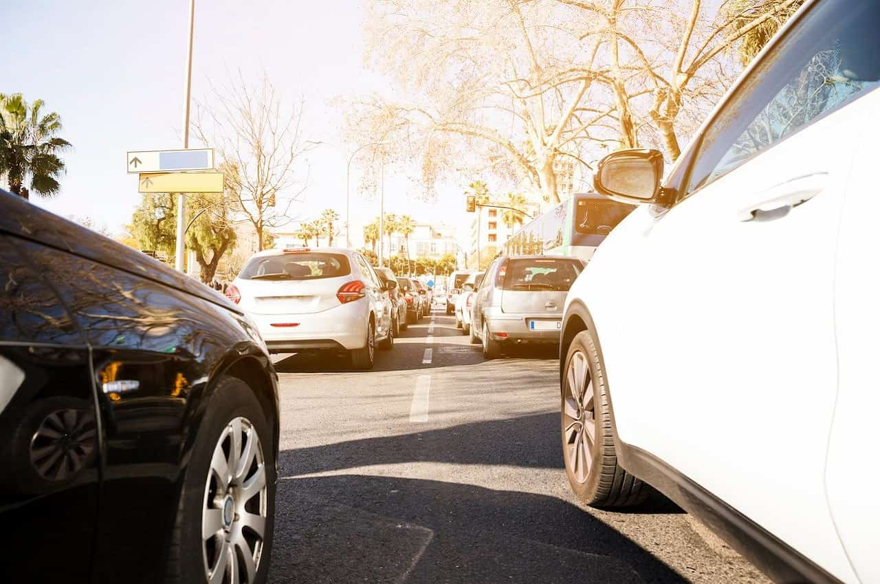 Fila de veículos estacionados no sol por conta do sinal vermelho.