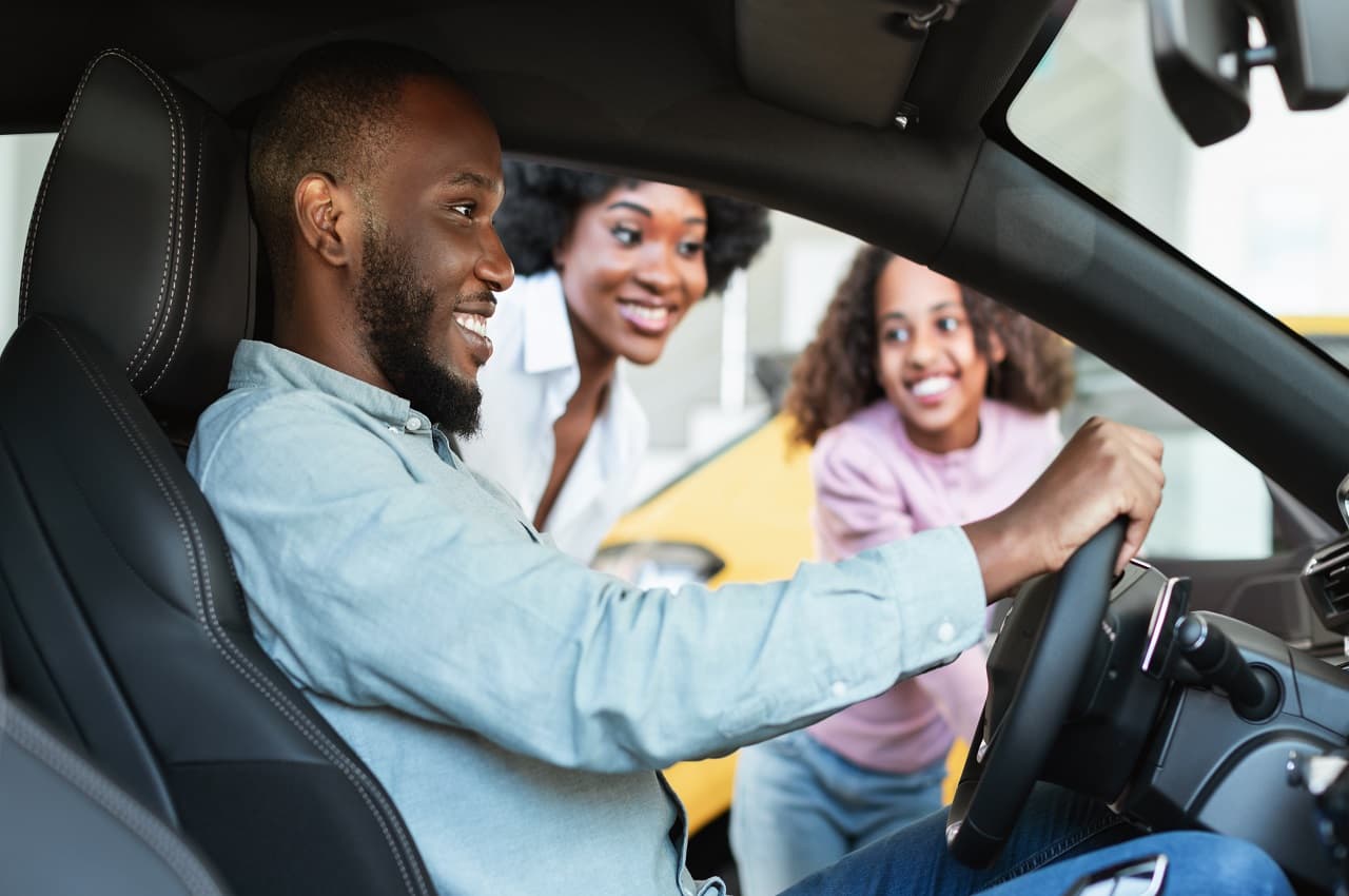 A imagem mostra um rapaz em seu carro e pessoas do lado de fora felizes por sua conquista.