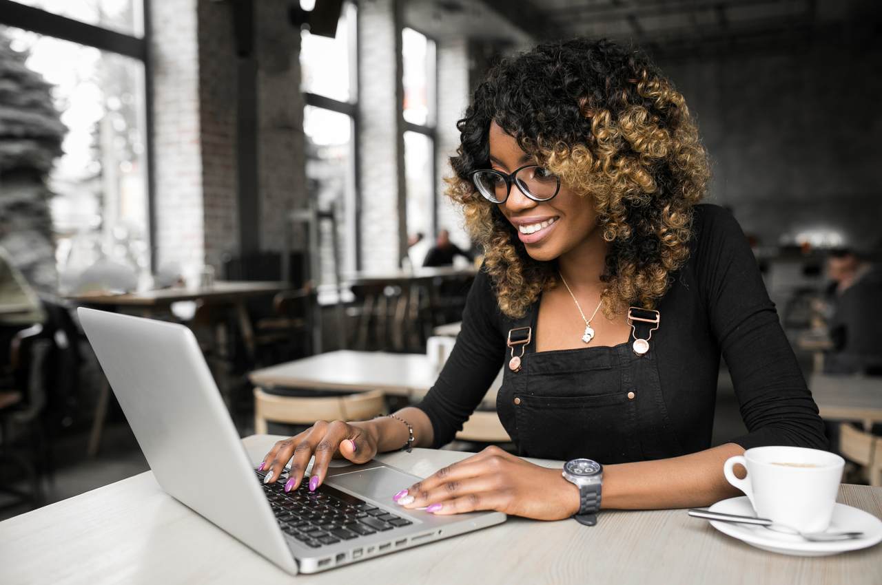 A imagem mostra uma mulher sorridente usando seu laptop.