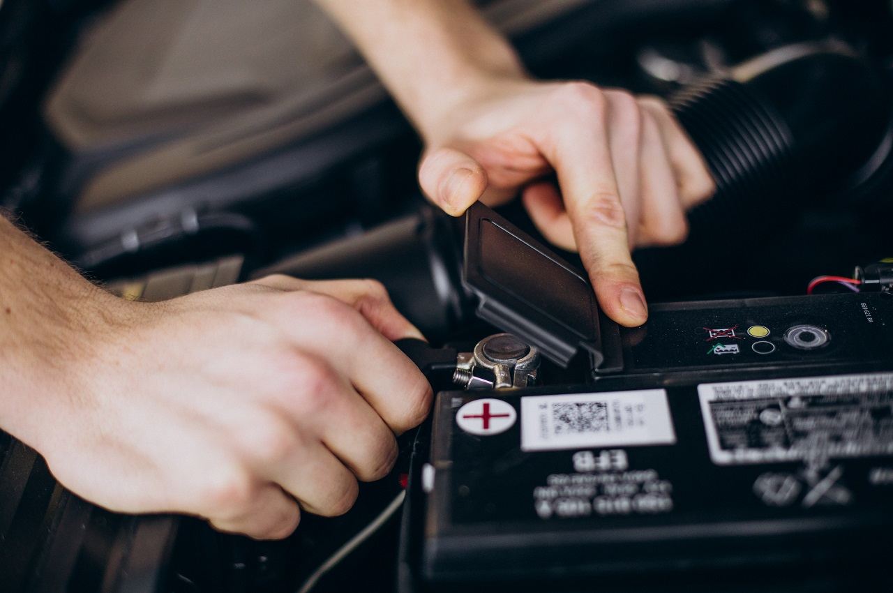 Mão abrindo sistema start-stop de carro próximo a bateria do veículo.