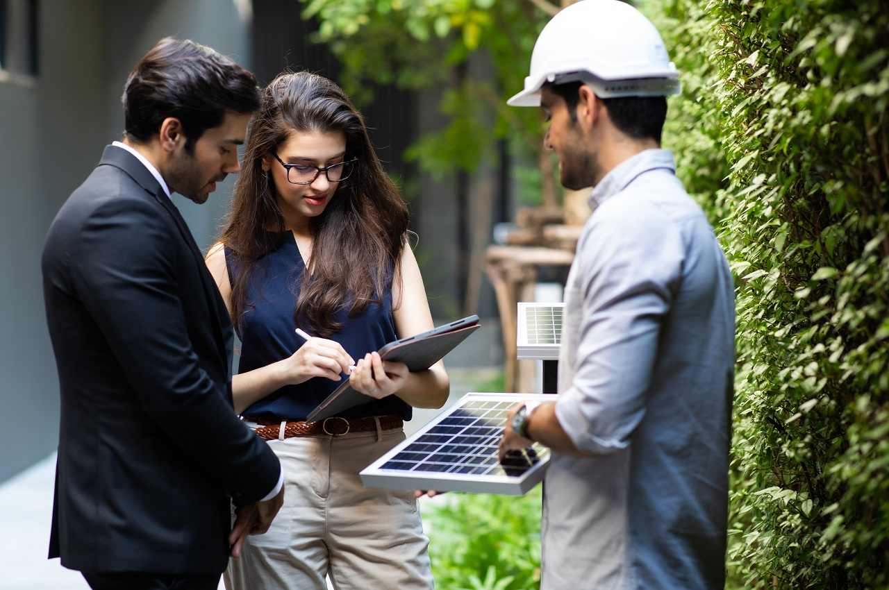 Homem e mulher com expressões concentradas conversando sobre energia solar no Brasil com outra pessoa que está vestindo EPIs de segurança para placas solares.