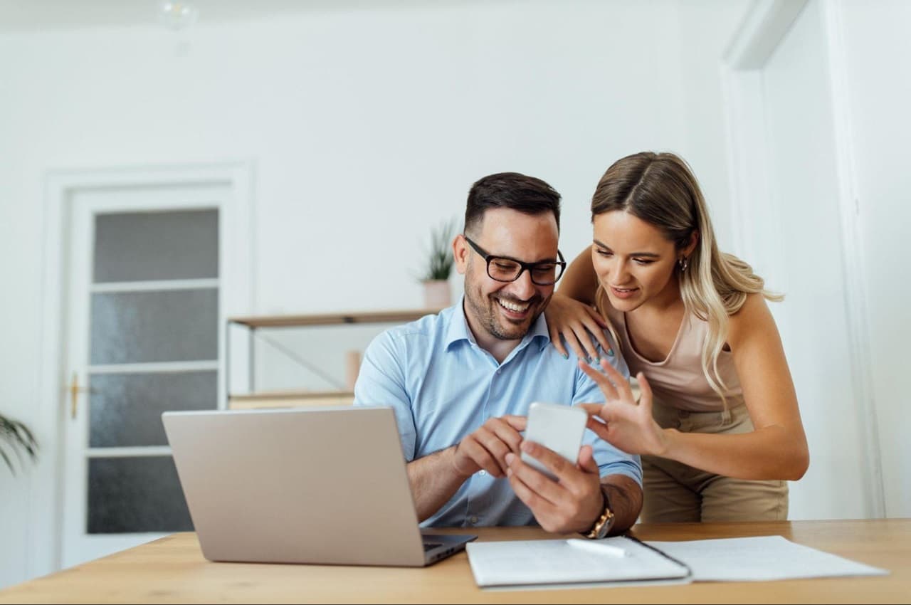 Homem e mulher sorridentes e abraçados pesquisando empréstimo pessoal no computador.