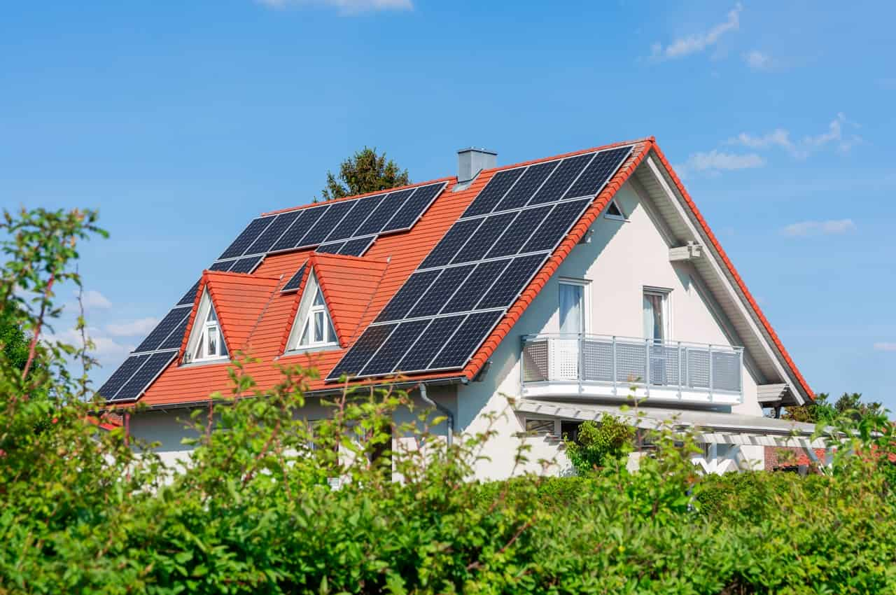 Casa sustentável com vegetação ao redor e painel solar no telhado.