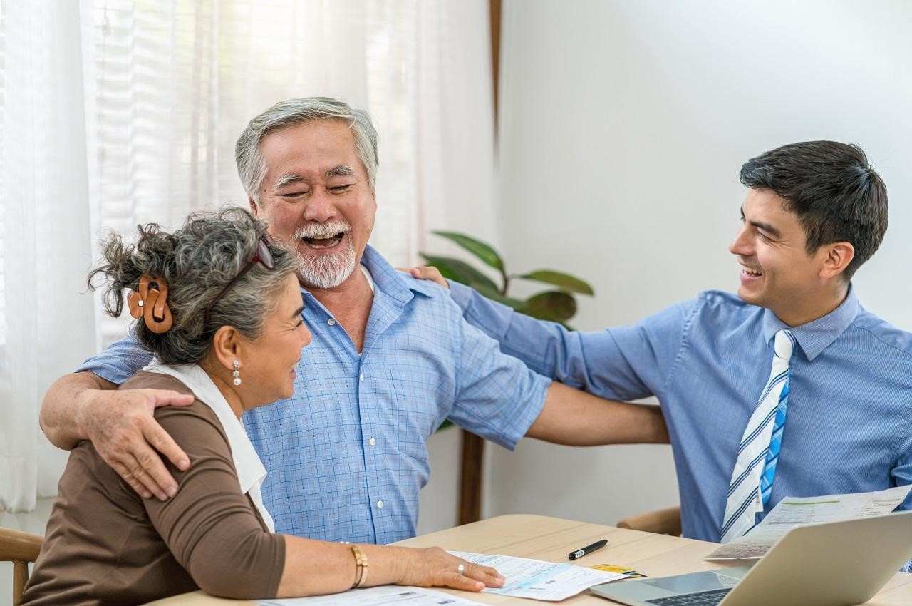 A imagem mostra uma família sorridente e se abraçando. Na imagem há três pessoas.