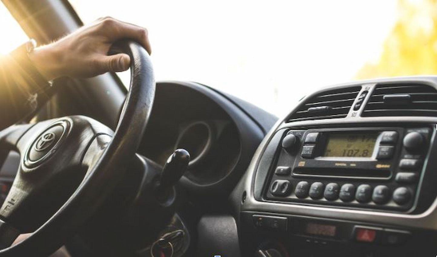 A imagem mostra uma pessoa com as mãos no volante dirigindo seu carro.