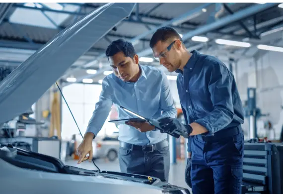 Dois homens inspecionam o motor de um carro em uma oficina mecânica, analisando detalhes.