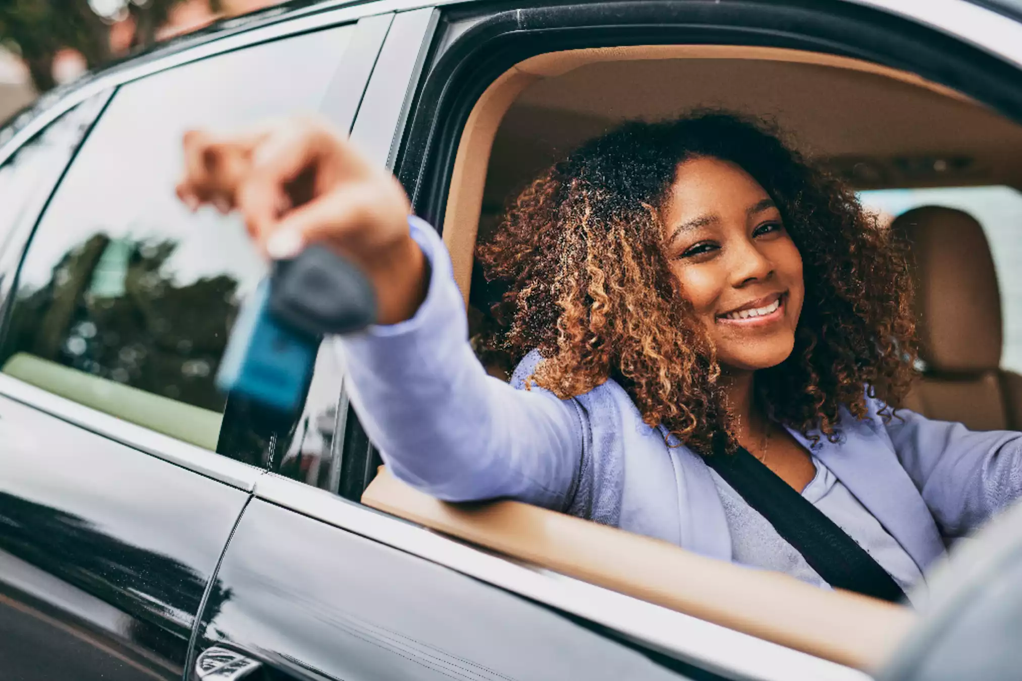 Uma mulher com cabelo cacheado sorri enquanto segura as chaves de um carro pela janela.