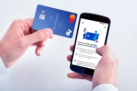 Pessoa segurando um cartão de crédito azul em uma mão e um smartphone em outra, parece estar realizando uma transação online.