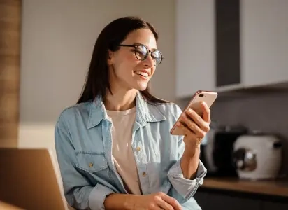 Na imagem há uma mulher de cabelos longos e escuros segurando um celular sorrindo.